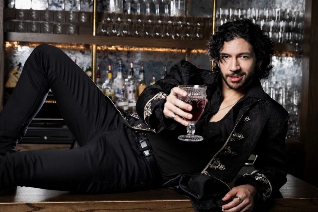 Performer dressed as Dracula holding a cocktail in a theatrical bar setting