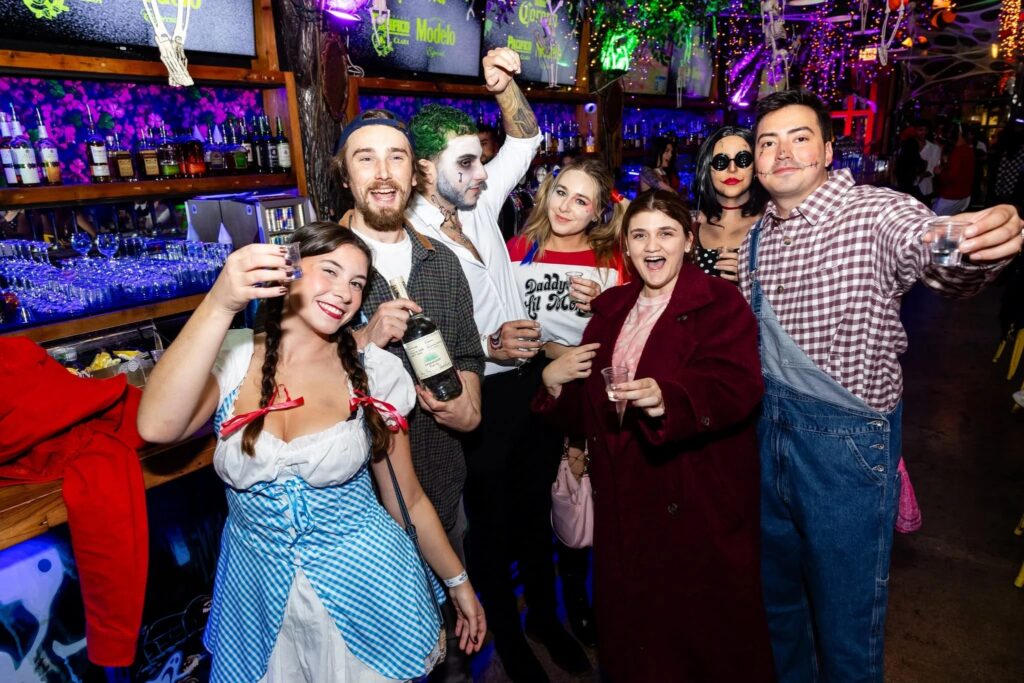 Halloween partygoers in costumes posing with drinks at a decorated Chicago bar.